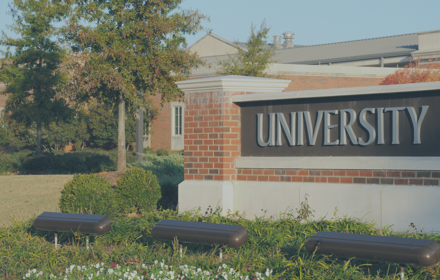 A brick sign reading "UNIVERSITY," with a background of trees and buildings, marks the gateway to higher education. Through initiatives like the Last Mile Fund, students are supported in reaching their academic goals.