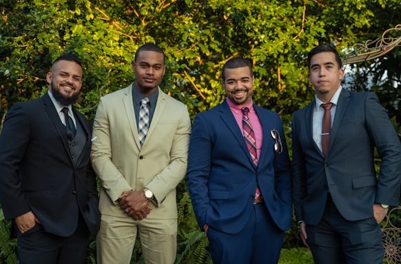 Four men in suits stand side by side outdoors in front of greenery, smiling for the camera as they celebrate new prosperity pathways.